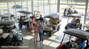 Customers browsing electric models in a modern golf cart dealership showroom with professional staff assistance.