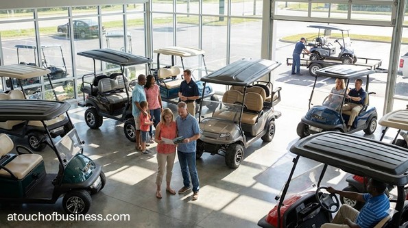 Customers browsing electric models in a modern golf cart dealership showroom with professional staff assistance.