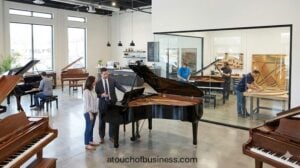 A grand piano business showroom with sales and technicians working in a glass workshop.