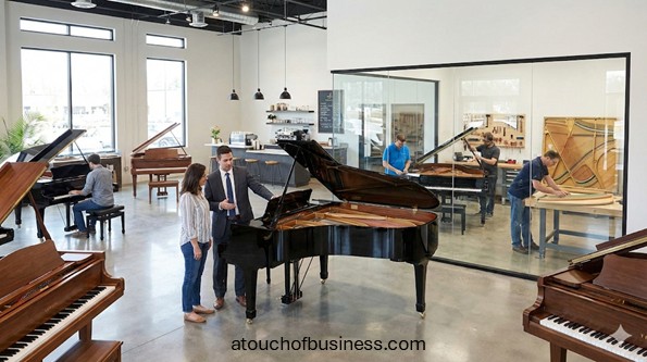 A grand piano business showroom with sales and technicians working in a glass workshop.