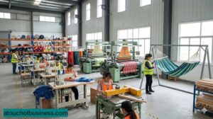 Workers operating industrial looms and sewing machines in a modern, professional hammock manufacturing factory facility.
