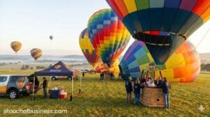 Hot air balloon business operation with colorful balloons launching in a scenic field at sunrise.
