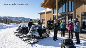 Customers preparing for a tour at a snowmobile rental business with a wooden lodge and snowy mountain backdrop.