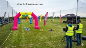 Several racing drones navigate through illuminated gates on a complex outdoor FPV racecourse.