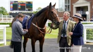 A trainer and owner discuss strategy in the paddock while a groom prepares a racehorse for competition.