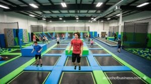Diverse kids and adults jumping on interconnected trampolines in a brightly lit indoor park.