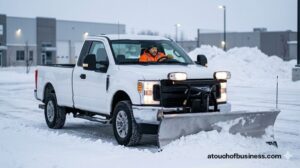 A snowplow attached to a modern pickup truck clears a snowy commercial parking lot.