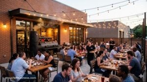 A modern BBQ restaurant patio at dusk with string lights, happy diners, and a large smoker operating near the brick building.