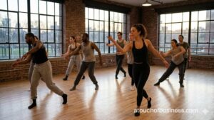 Dancers follow a teacher's lead in a modern industrial dance studio with large windows.